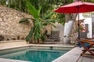 a swimming pool with a red umbrella and a table and chair at Casa Armadillo, colonial house with pool in Mérida