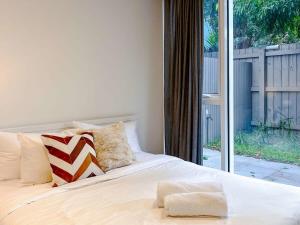 uma cama branca com almofadas e uma porta de vidro deslizante em BPM Brighton APT with Garden LG1 em Melbourne