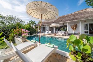 a pool with chairs and an umbrella next to a house at Villa Moana Poe Uluwatu in Uluwatu