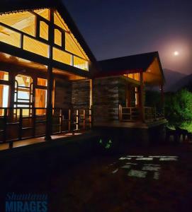 une maison en rondins la nuit avec la lune derrière elle dans l'établissement Cliff Haven Tirthan, à Banjār