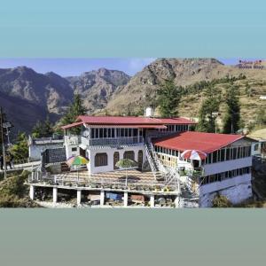 a white building with a red roof with mountains in the background at Gulab - B Homestay in Dehradun