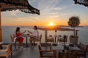 a couple sitting at a table in front of a sunset at Petit Palace Suites in Fira