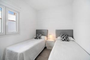 two beds in a white room with a window at Dafer Piscina Privada in Chiclana de la Frontera