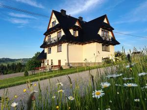 a house with a black roof and a field of flowers at Pokoje u Hani - sauna, balia z hydromasażem in Bukowina Tatrzańska