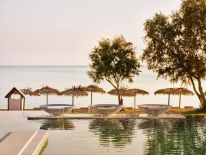 Kalamákion的住宿－Casa Marron Grecotel All Inclusive Resort，海滩上带桌子和遮阳伞的游泳池