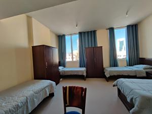 Habitación con 3 camas, silla y ventanas. en Oasis Hostel, en Abu Dabi