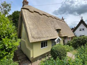 une petite maison jaune avec un toit de chaume dans l'établissement Buttercup Cottage, Hartest, à Hartest
