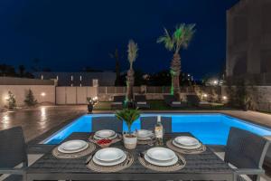 a dining table and chairs next to a swimming pool at night at Sun White Villas in Laganas