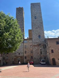 a woman walking in front of a castle with two towers at A La Casa Dei Potenti in San Gimignano