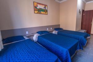 drie bedden in een kamer met blauwe lakens bij Alfa Hotel Vespasiano in Vespasiano