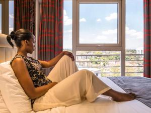 a woman sitting on a bed looking out a window at ibis Styles - Nairobi, Westlands in Nairobi