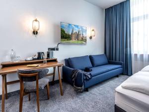 een hotelkamer met een bureau en een blauwe bank bij Mercure Hotel Luebeck City Center in Lübeck