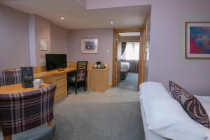a room with a couch and a desk with a television at The Suites Hotel & Spa Knowsley - Liverpool by Compass Hospitality in Knowsley