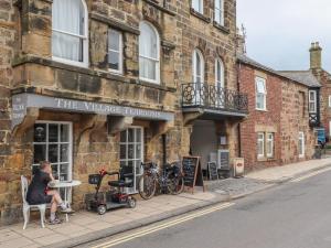 a woman sitting at a table in front of a building at Five Bells Cottage in Alnmouth