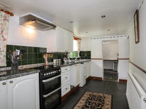 a kitchen with white cabinets and black appliances at Hendy Cottage in Llanbedr