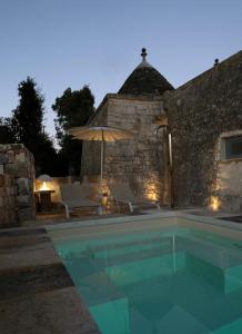 ein Pool mit Sonnenschirm und Stühlen und ein Haus in der Unterkunft TRULOCO NUZZI - LUXURY DOMUS in Locorotondo