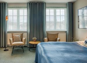a bedroom with two chairs and a bed and windows at Color Hotel Skagen in Skagen