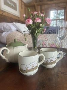 three tea cups and a vase with flowers on a table at Whittlewood Shepherd's Hut in Silverstone, Cosy, Rural, Views in Silverstone