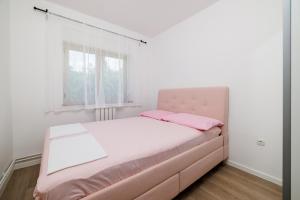 a white bedroom with a pink bed with pink pillows at Apartman Mediteran in Crikvenica