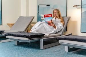 a woman sitting on a bed reading a book at Das Ahlbeck Hotel & SPA in Ahlbeck