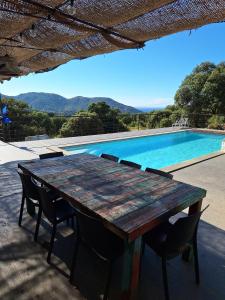 una mesa de madera y sillas junto a una piscina en San Quilico - Maison climatisée piscine vue mer, en Aregno