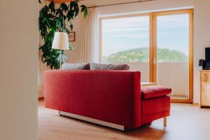 ein rotes Sofa im Wohnzimmer mit einem großen Fenster in der Unterkunft Lindenhaus in Zwiesel