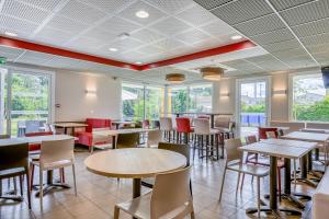 ein Restaurant mit Tischen, Stühlen und Fenstern in der Unterkunft ACE Hôtel Bordeaux Carbon Blanc in Carbon-Blanc