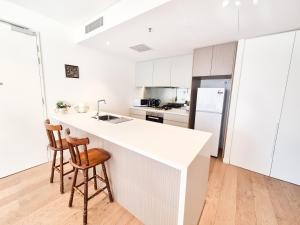 a white kitchen with a counter and two stools at Cozy Apartment at St Leonard in Sydney