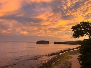einen Sonnenuntergang über einem Strand mit Felsen im Wasser in der Unterkunft Huellas in Arecibo