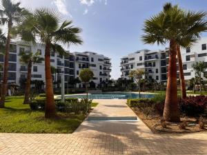 a resort with a pool and palm trees and buildings at Appartement de Luxe Costa-Mar Martil Tetouan in Martil