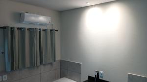 ein Bad mit einem Duschvorhang und einem Licht an der Wand in der Unterkunft LOCANDA DA SERRA - Aptos Mobiliados e Suítes por Temporada in Barra do Garças