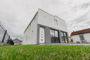 a white house with large windows on a lawn at Apartmani Rosa in Nevesinje