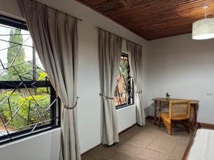 a room with two windows and a table and a desk at Njombe Cozy House in Njombe