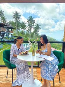 twee vrouwen zitten aan een tafel te lezen bij Bintana sa Paraiso Binunsaran in Mambajao