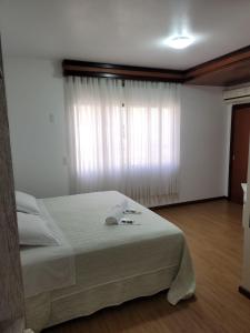 a bedroom with a large white bed with a window at Hotel Vila Germânica in Blumenau