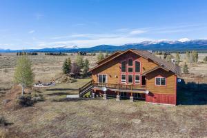 Una casa de troncos en un campo con montañas al fondo en Hint of Heaven by KABINO HotTub Air Hockey Firepit Fishing Trails Yellowstone Free WiFi, en Island Park