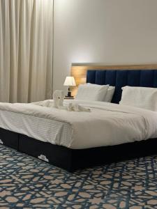 een groot bed met witte lakens en een blauw hoofdeinde bij ضيف بارك للأجنحة الفندقية in Dawadmi