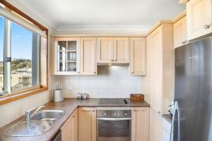 eine Küche mit Holzschränken und einem Kühlschrank aus Edelstahl in der Unterkunft Scenic Beachside Apartment, near Bar & Restaurant in Terrigal