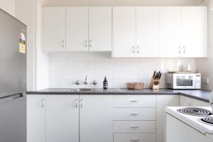 シドニーにあるSunny Apartment in Quiet and Green Neighbourhoodの白いキッチン(白いキャビネット、電子レンジ付)