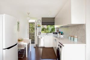 a kitchen with white cabinets and a table in it at Treetop Retreat Five Minute Stroll To The Beach in Sydney