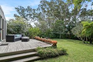 een achtertuin met een houten terras met een bank en een tuin bij Immaculate Beachside Home with Fireplace and Patio in Bateau Bay