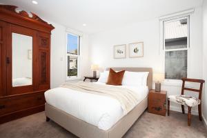 a white bedroom with a bed and a chair at Spacious 3-Bed Family House with Courtyard in Sydney