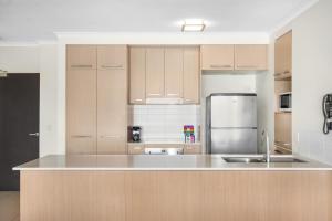 a kitchen with wooden cabinets and a stainless steel refrigerator at Lakeside Family Oasis with Pool, Gym and Balcony in Gold Coast
