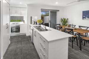 a kitchen with white cabinets and a dining room with a table at Charming 3-Bed House with Patio near Sport Stadium in Brisbane