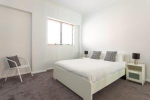 a white bedroom with a white bed and a chair at Chic Unit with Rooftop Terrace near Sights & Shops in Sydney