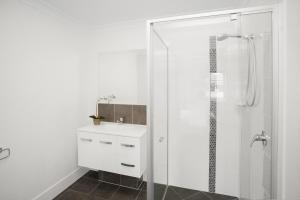 a white bathroom with a shower and a sink at Charming 3-Bed House with Patio near Sport Stadium in Brisbane