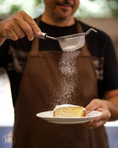 um homem a espalhar açúcar em pó num pedaço de bolo em Corte Boero Bed&Breakfast em Capoterra
