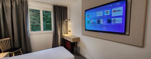 Habitación de hotel con TV de pantalla plana en la pared en Anaïs Hôtel Bourges Nord Saint-Doulchard en Bourges