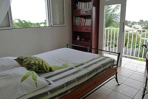 Bett in einem Schlafzimmer mit Balkon in der Unterkunft Appartement de charme dans villa avec piscine in Saint-François