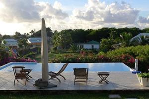 ein Pool mit Stühlen, Sonnenschirm und Surfbrett in der Unterkunft Appartement de charme dans villa avec piscine in Saint-François